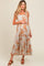 woman wearing a light gray floral print maternity maxi dress with ruffled straps and holding her baby bump