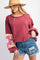 woman wearing a burgundy oversized sweatshirt with a floral design on the sleeves and distressed denim shorts