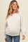 woman wearing a light gray maternity sweatshirt with a wide neckline and long sleeves, smiling at the camera