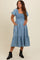 woman wearing a light blue maternity dress with short puff sleeves, smocked bodice, and tiered skirt, showcasing a baby bump