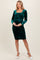 woman wearing a dark green velvet maternity dress with long sleeves and gathered detailing, showing her baby bump