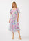 woman wearing a flowing floral midi dress with short sleeves and a v-neckline, standing against a white background