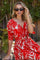 woman wearing a red and white patterned wrap dress with short sleeves and sunglasses in a tropical setting