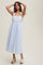 woman wearing a light blue striped midi dress with floral bodice and tie straps, standing with hands raised above her head