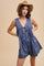 woman wearing a blue floral patterned romper with a v-neck and a tie detail, posing with a straw hat
