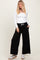 woman wearing a white long sleeve top and black wide-leg pants with side pockets and a drawstring waist