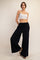 woman wearing a white cropped tank top and black wide leg pants, standing with one leg slightly bent