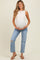 woman wearing a beige sleeveless maternity top and distressed blue jeans, holding her baby bump