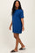 woman wearing a short-sleeve blue t-shirt dress and black slide sandals, smiling while walking