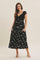 woman wearing a black floral midi dress with a crochet top and pockets, standing against a neutral background