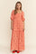 woman wearing a coral maxi dress with floral embroidery and puffed sleeves, standing against a neutral background