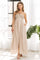 woman wearing a beige maxi dress with a crochet bodice and side pockets, standing in a sunlit room with greenery