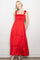 woman wearing a red maxi dress with smocked bodice and bow-tie straps, posing against a neutral background