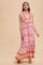 woman wearing a pink floral maxi dress with a tie at the waist and orange accents, posing against a light background