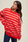 woman wearing a red and white striped oversized sweater with a ribbed neckline and side slit, paired with navy pants