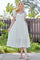 woman wearing a white midi dress with puff sleeves and a tiered skirt, standing outdoors in a sunny setting