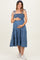 woman wearing a blue smocked maternity dress with tiered skirt and tie straps, gently holding her baby bump