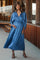 woman wearing a blue pleated maternity dress with a deep v-neckline, showing her baby bump and smiling