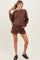 woman wearing a chocolate brown long sleeve maternity sweatshirt and matching shorts, styled casually with sandals