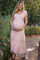 woman wearing a light pink maternity maxi dress with smocking and ruffle sleeves, holding her baby bump in a garden setting