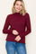 woman wearing a burgundy ribbed long sleeve top with scalloped edges and standing with a smile