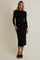 woman wearing a black long sleeve fitted midi dress with a draped neckline and styled with black slide sandals