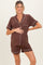 woman wearing a brown short sleeve maternity pajama set with white piping and holding her baby bump