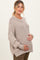 woman wearing a beige knitted maternity sweater and gently cradling her baby bump