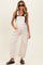 woman wearing a light beige maternity overall with wide leg and side pockets, styled with a black tank top and sunglasses