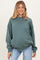woman wearing a green oversized sweatshirt and light blue jeans, showcasing her baby bump