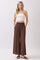 woman wearing a white strapless top and brown wide-leg pants, standing with hands in pockets
