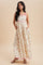 woman wearing a cream floral maxi dress with pink accents and pockets, standing against a neutral background
