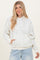woman wearing a cream hoodie with a floral print and front pocket, paired with light blue jeans