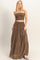 woman wearing a brown strapless smocked top and tiered maxi skirt, standing in a relaxed pose