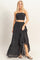 woman wearing a black smocked crop top and a black tiered maxi skirt with a high-low hemline and heeled sandals