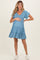 woman wearing a blue patterned maternity dress with short sleeves and a tiered skirt, holding her baby bump