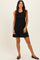 woman wearing a black pleated sleeveless dress with a fitted bodice and flared skirt, standing with one hand on her hip