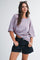 woman wearing a pink and purple striped oversized t-shirt and dark denim shorts, smiling and posing with hands on hips