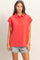 woman wearing a red oversized polo shirt with short sleeves and button details, paired with distressed denim shorts
