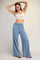 woman wearing a light blue high-waisted wide leg pants and a white crop top, posing with her hands above her head