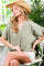 woman wearing a light green oversized blouse with a v-neck and white shorts, accessorized with a straw hat