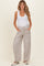 woman wearing a white tank top and light striped maternity pants with pockets, standing casually