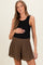woman wearing a black ribbed maternity tank top and brown elastic waist shorts, holding her baby bump