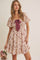 woman wearing a floral smocked mini dress with puff sleeves and a tie detail, holding a bouquet of dried flowers