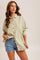 woman wearing a light green striped oversized shirt and denim shorts, posing casually