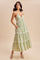 woman wearing a light green tiered maxi dress with spaghetti straps and pockets, standing on a tan background