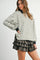 woman wearing a white and black striped oversized sweatshirt paired with a black and grey plaid ruffled mini skirt