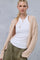 woman wearing a beige cable-knit cardigan over a white tank top and olive green pants, styled with layered necklaces