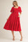 woman wearing a red midi dress with short puff sleeves, square neckline, and decorative patterns, standing in a slight pose