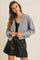 woman wearing a gray cropped cardigan over a black tank top and black faux leather shorts